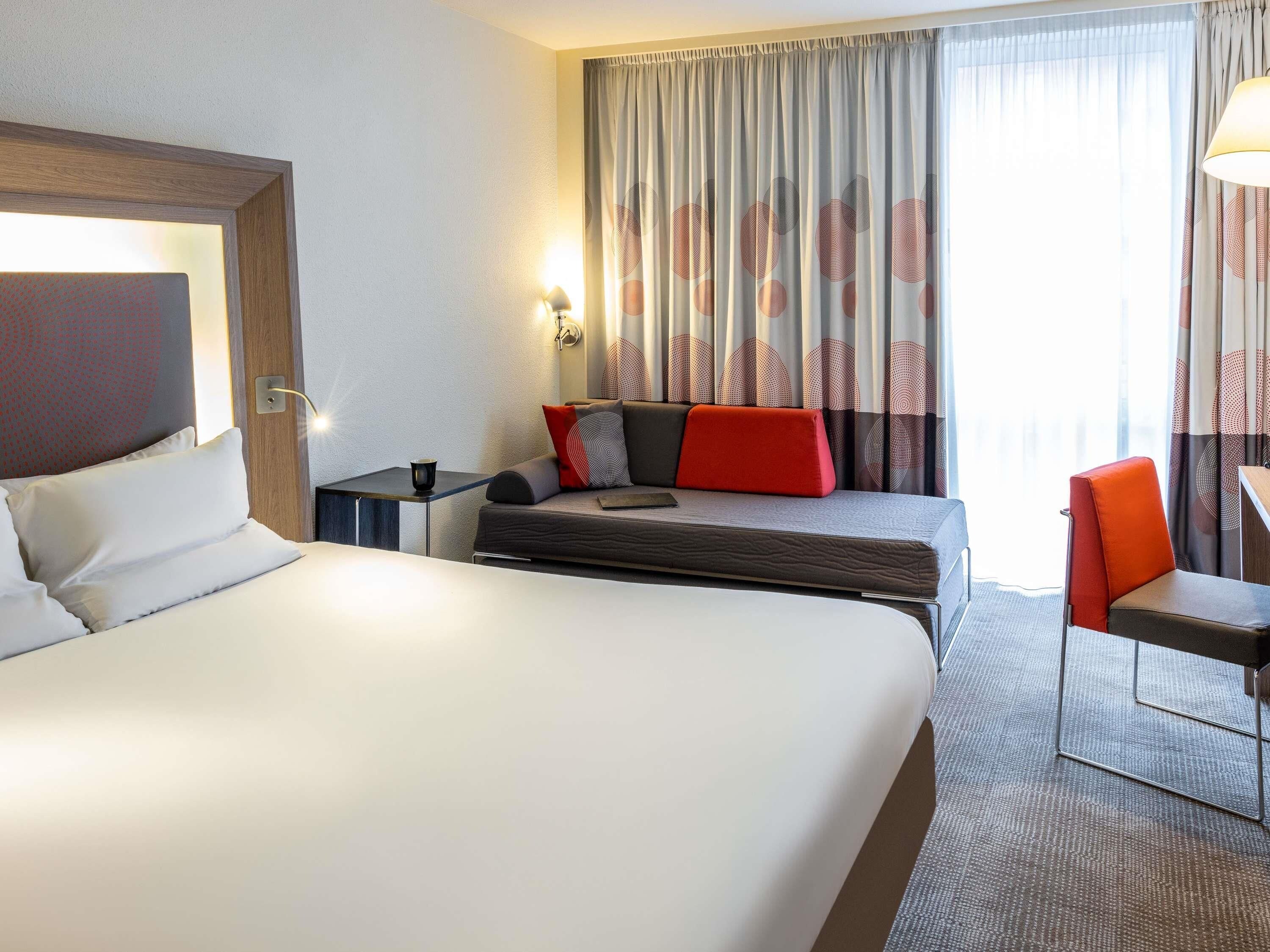 A hotel room with a large bed, a desk, a chair, and a window with curtains.