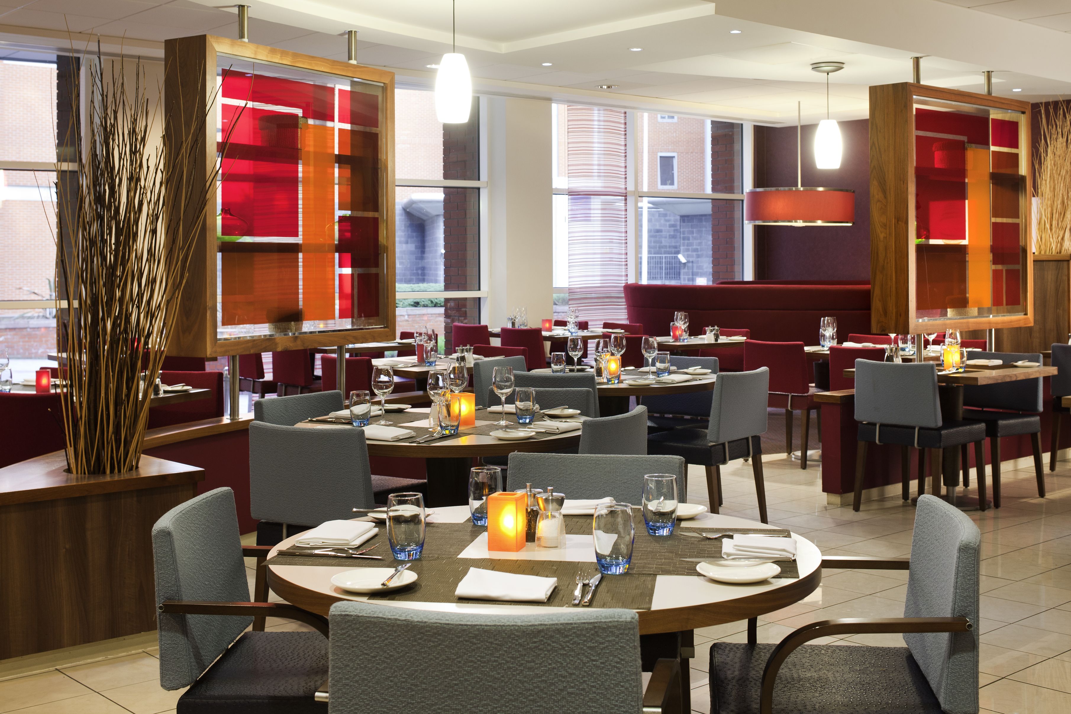 A restaurant with multiple tables set for dining, featuring red and white decor, and large windows providing natural light.