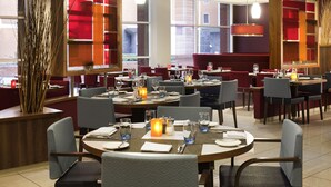 A restaurant with multiple tables set for dining, featuring red and white decor, and large windows providing natural light. - Novotel Leeds Centre (Leeds)