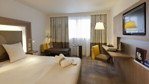 A hotel room with a large bed, a desk with a laptop, a chair, a small table, and a TV mounted on the wall. - Novotel Leeds Centre (Leeds)
