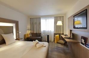 A hotel room with a large bed, a desk with a laptop, a chair, a small table, and a TV mounted on the wall. - Novotel Leeds Centre (Leeds)