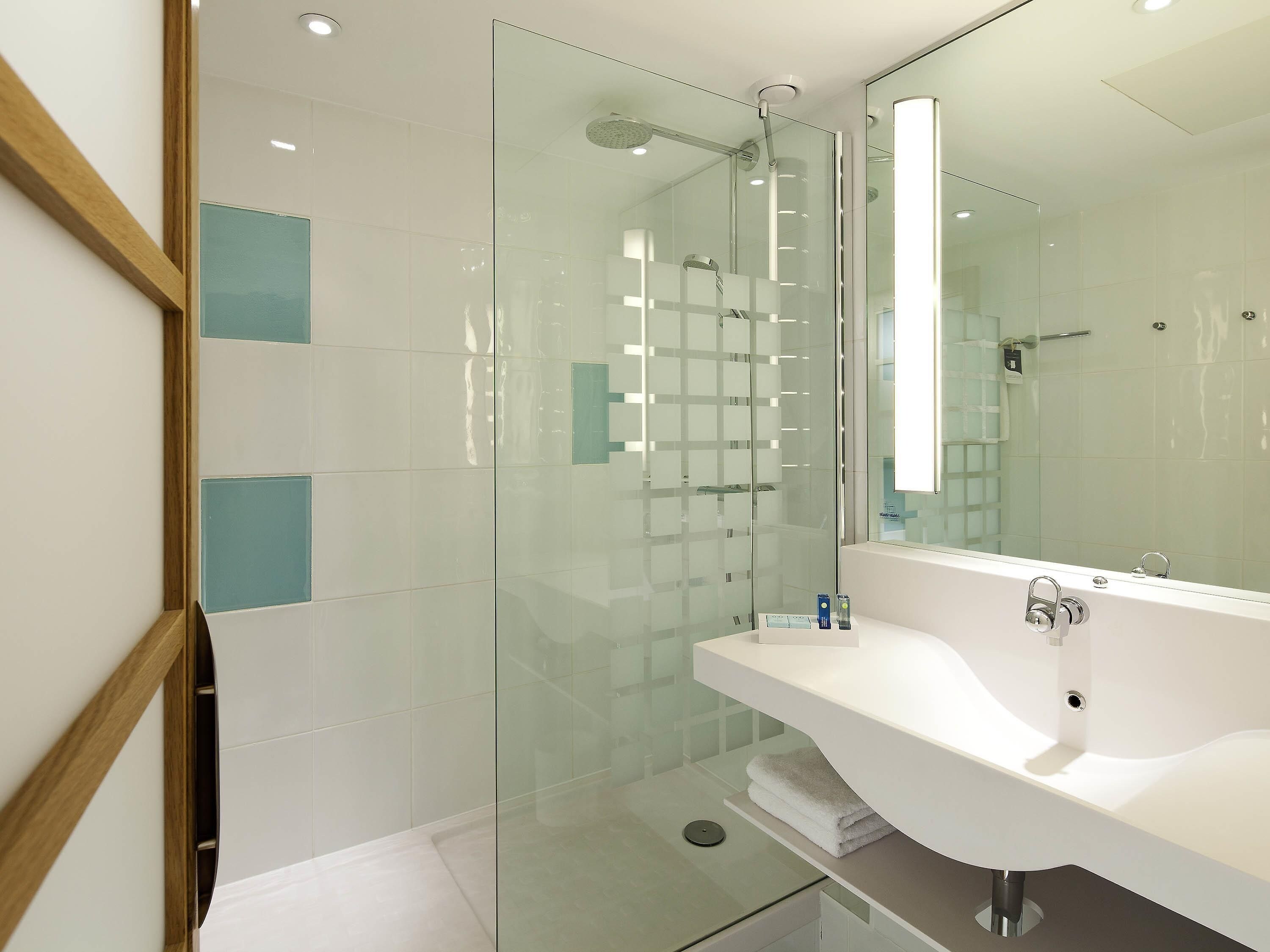 A modern bathroom with a glass shower enclosure, a white sink, and a large mirror.