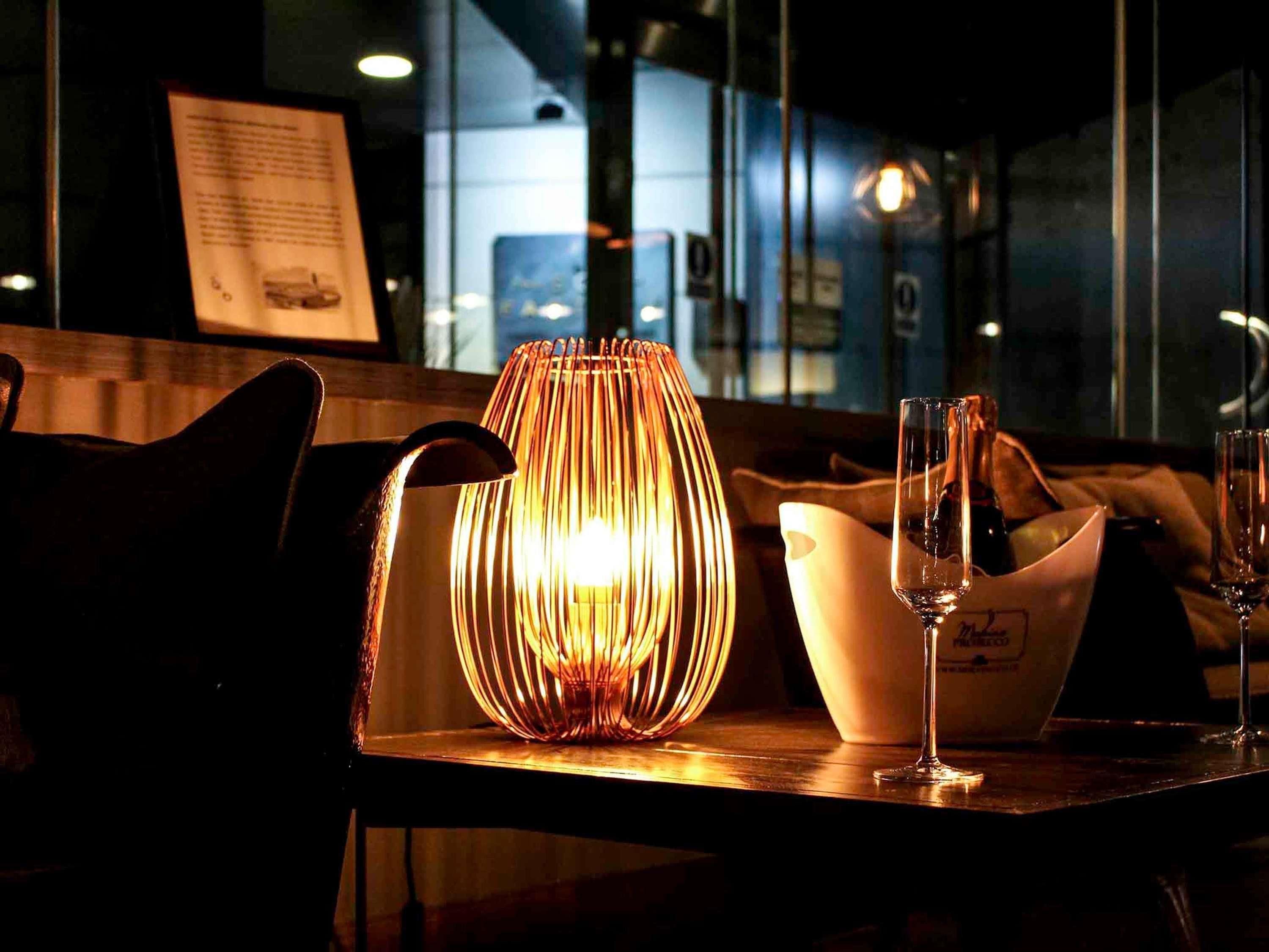 A dimly lit bar area with a candle holder, a menu board, and glasses on a table.