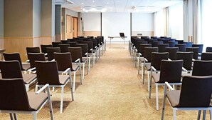 A conference room with rows of chairs, a projector screen, and a table with a laptop. - Novotel Leeds Centre (Leeds)