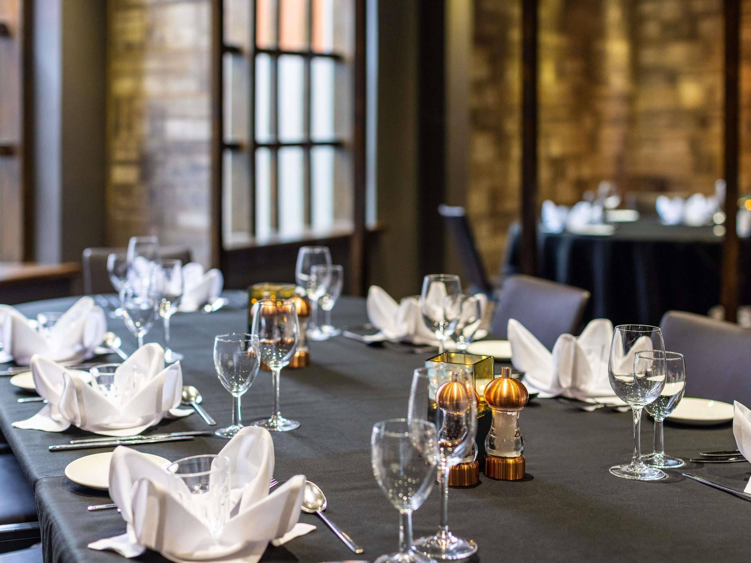 A restaurant table set with wine glasses, plates, and cutlery, with a dark tablecloth and a decorative centerpiece.