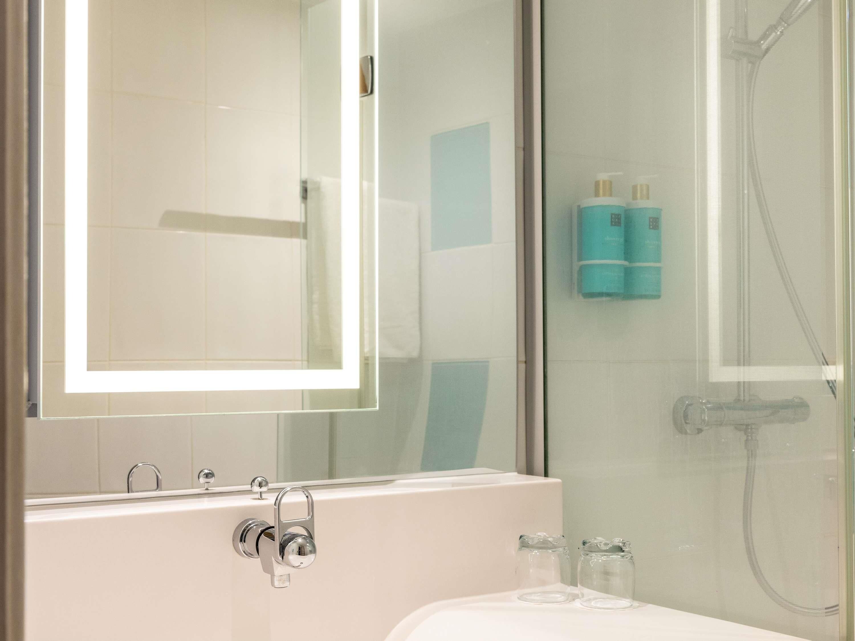 A modern bathroom with a glass shower enclosure, a white bathtub, and a mirror above the sink.
