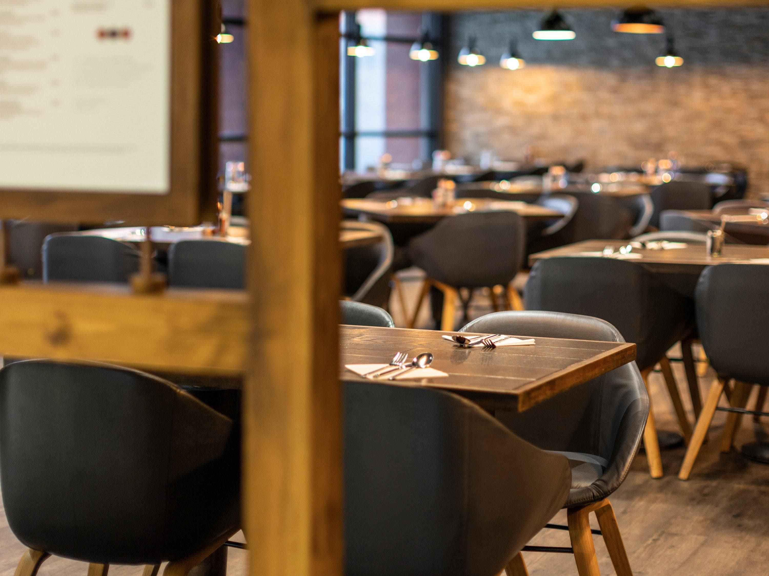A restaurant interior with multiple tables and chairs, wooden flooring, and pendant lighting.