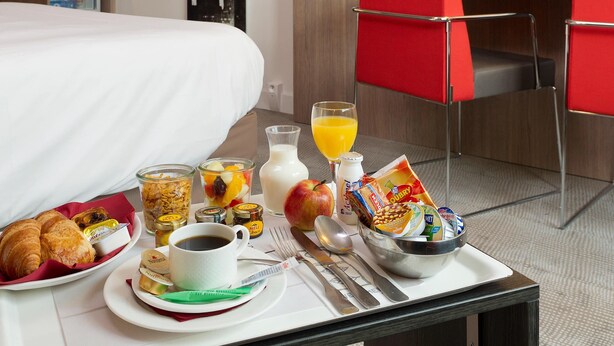 A hotel room with a bed, breakfast tray, red chairs, and a refrigerator. - Novotel Leuven Centrum (Leuven)