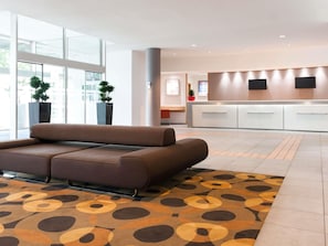 A modern lobby with a sofa, a reception desk, and large windows. - Novotel Leuven Centrum (Leuven)