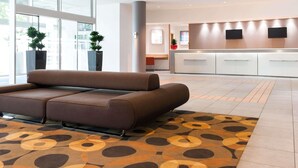 A modern lobby with a sofa, a reception desk, and large windows. - Novotel Leuven Centrum (Leuven)