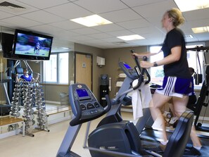 A gym with treadmills, a weight rack, and a television displaying a sports event.