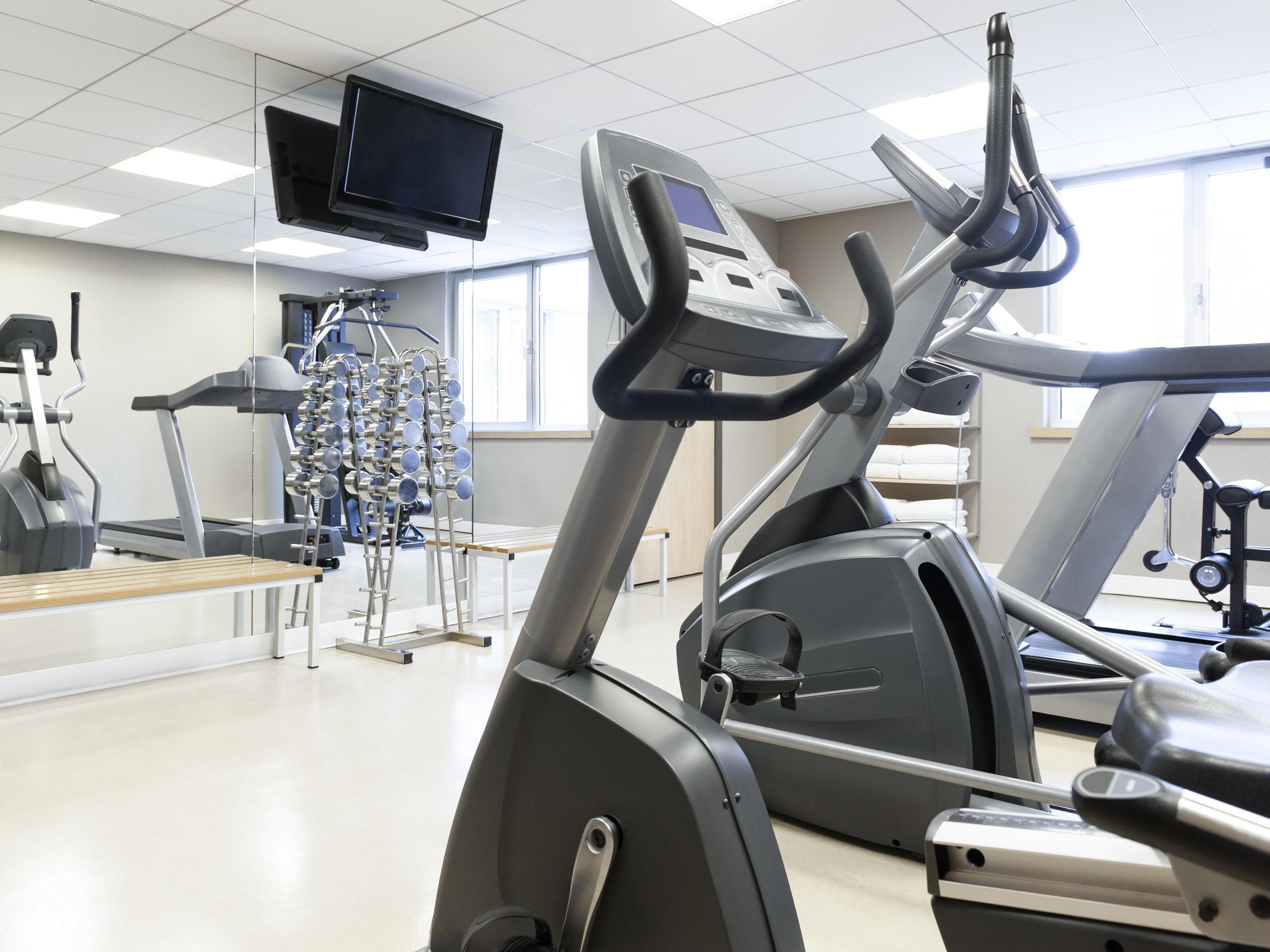 A gym with treadmills, elliptical machines, and a television mounted on the ceiling.