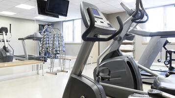 A gym with treadmills, elliptical machines, and a television mounted on the ceiling.