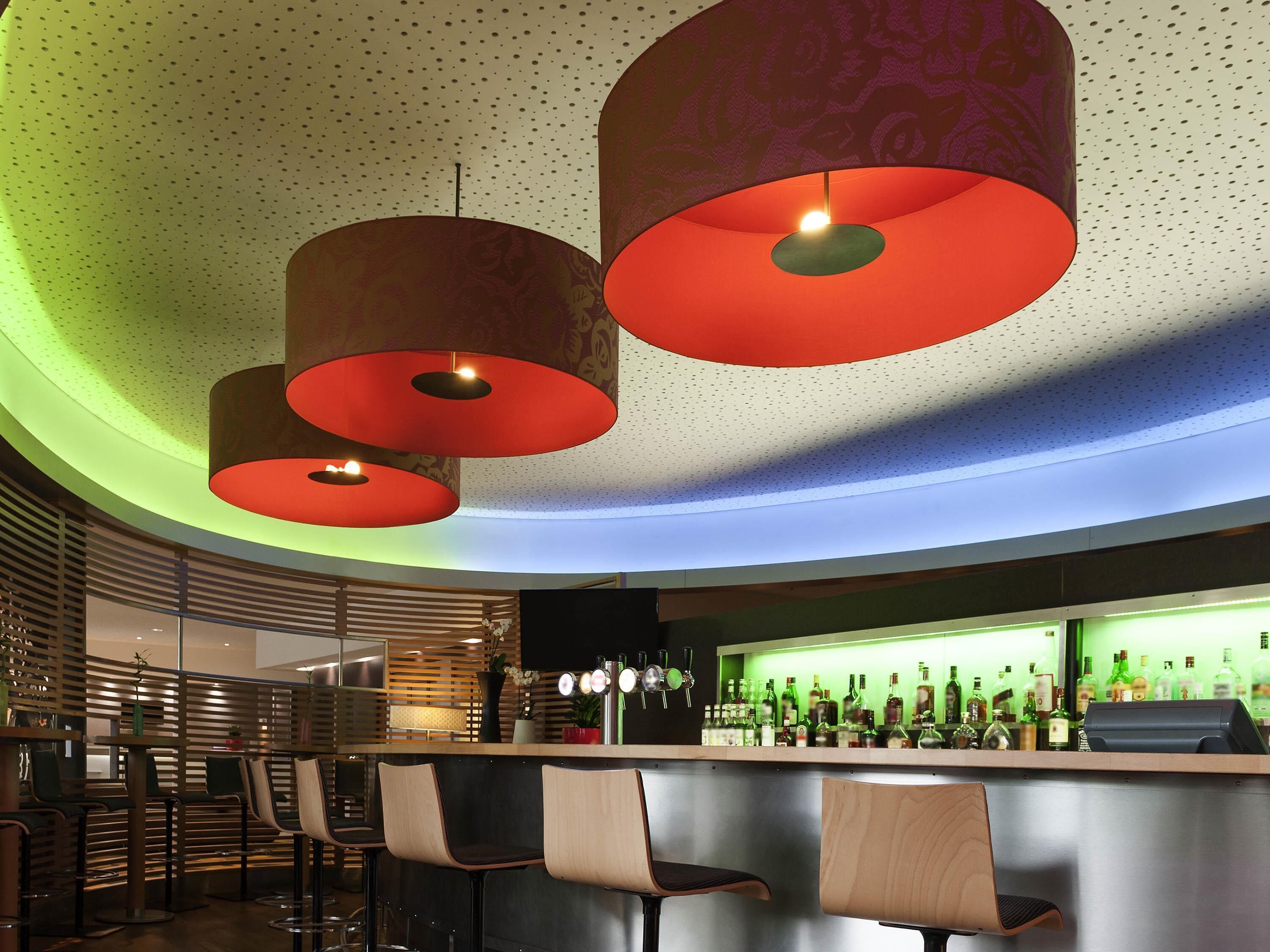 A modern bar area with a curved ceiling, multiple hanging red pendant lights, and a bar counter with stools.