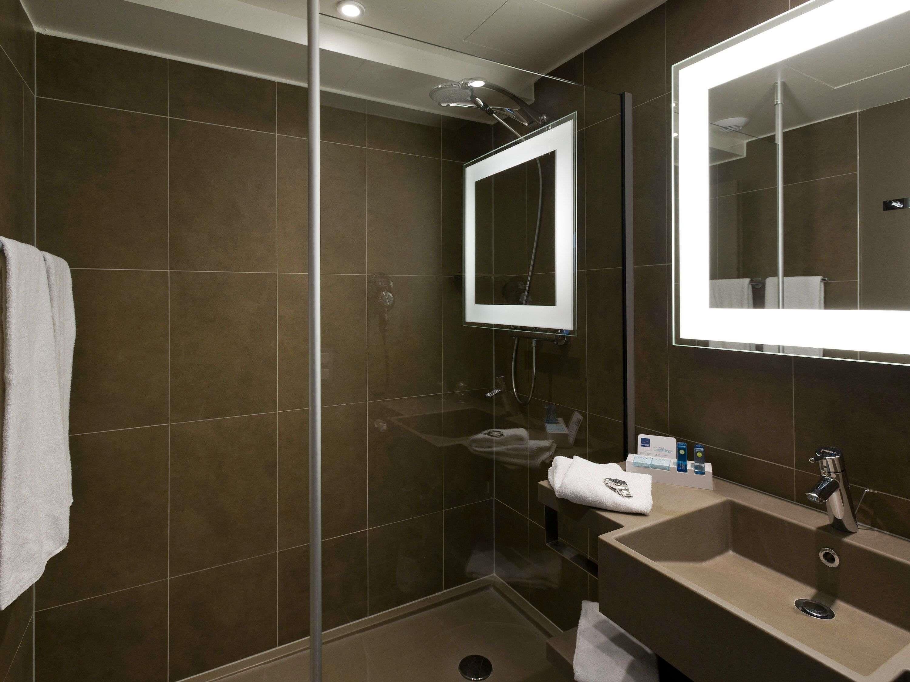 A modern bathroom with a glass-enclosed shower, a large mirror, and a sink with a towel.