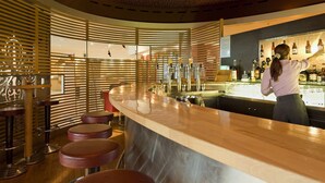 A bar area with a counter, stools, and a bartender. - Novotel Leuven Centrum (Leuven)