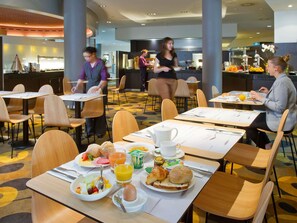 Comedor de hotel con mesas preparadas para el desayuno, incluyendo platos de comida, bebidas y productos para el desayuno.