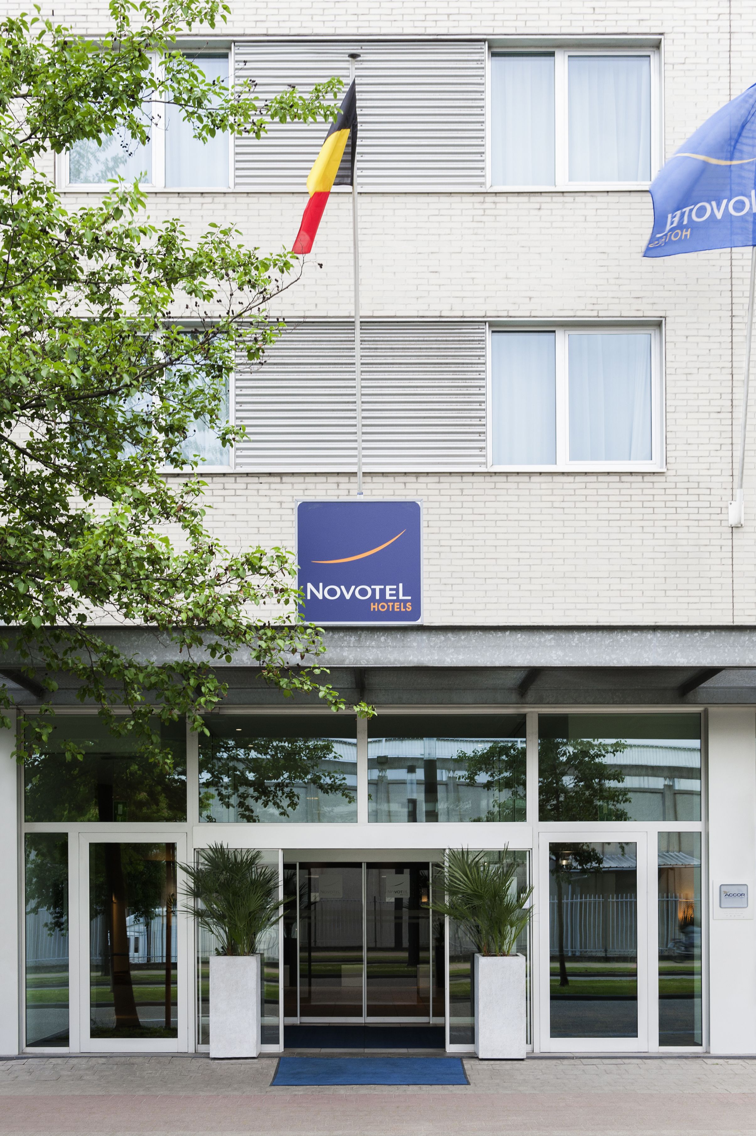 A Novotel hotel entrance with a flag, large windows, and a blue mat at the door.