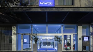 A hotel entrance with a blue sign, glass doors, and a blue carpet. - Novotel Leuven Centrum (Leuven)