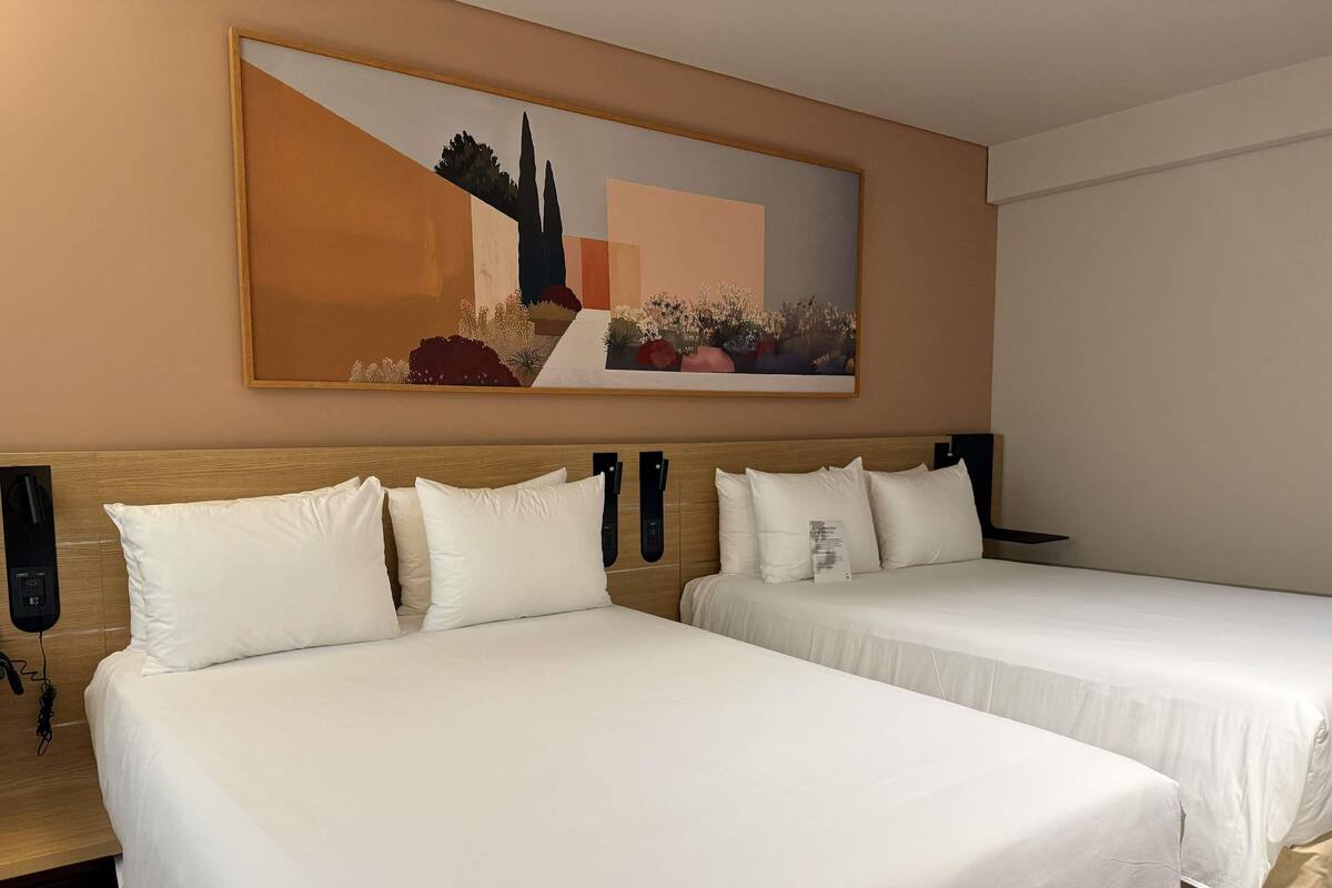 Una habitación de hotel con dos camas, un cuadro en la pared y un cabecero de madera.