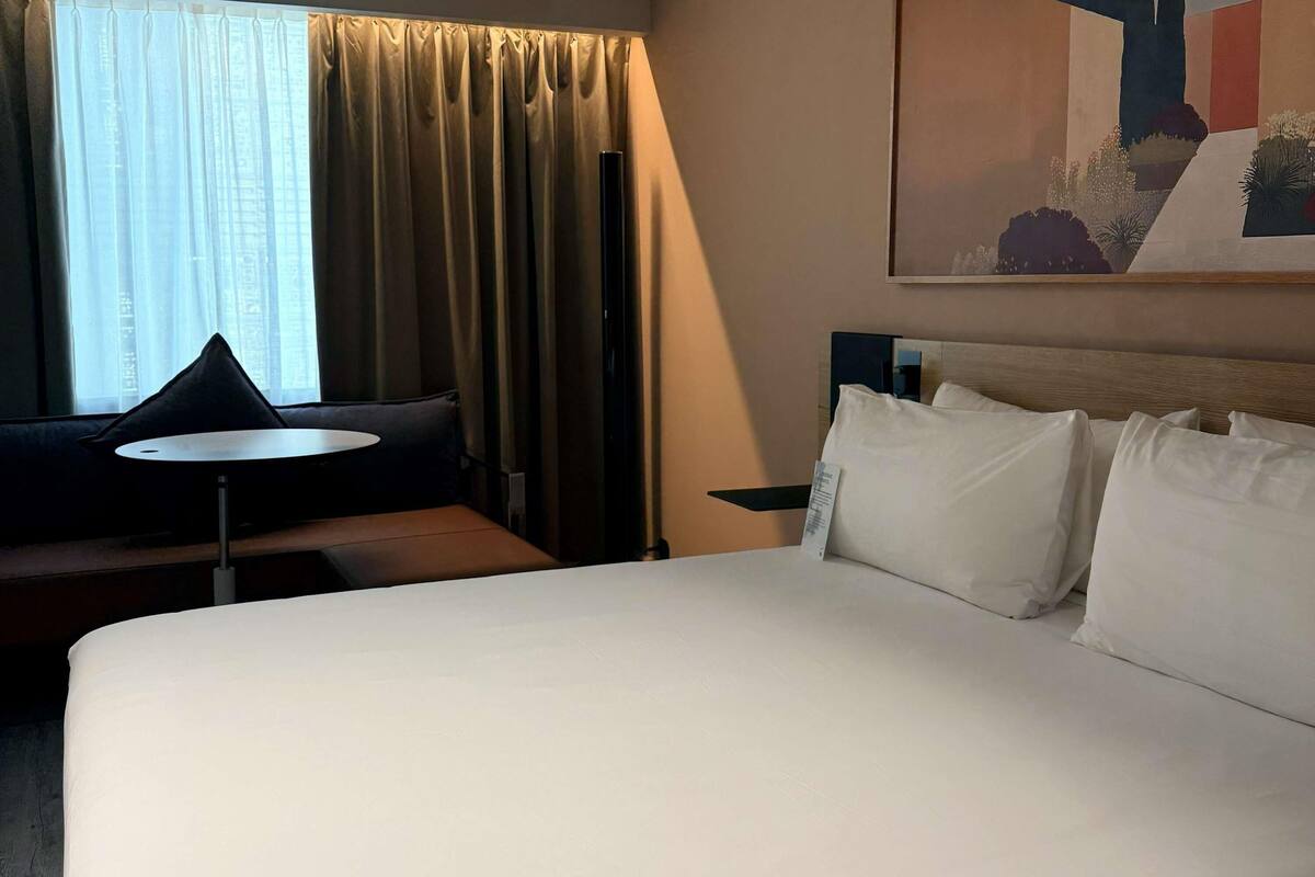 Habitación de hotel con una cama grande, una mesita redonda pequeña, un sofá y un cuadro en la pared.