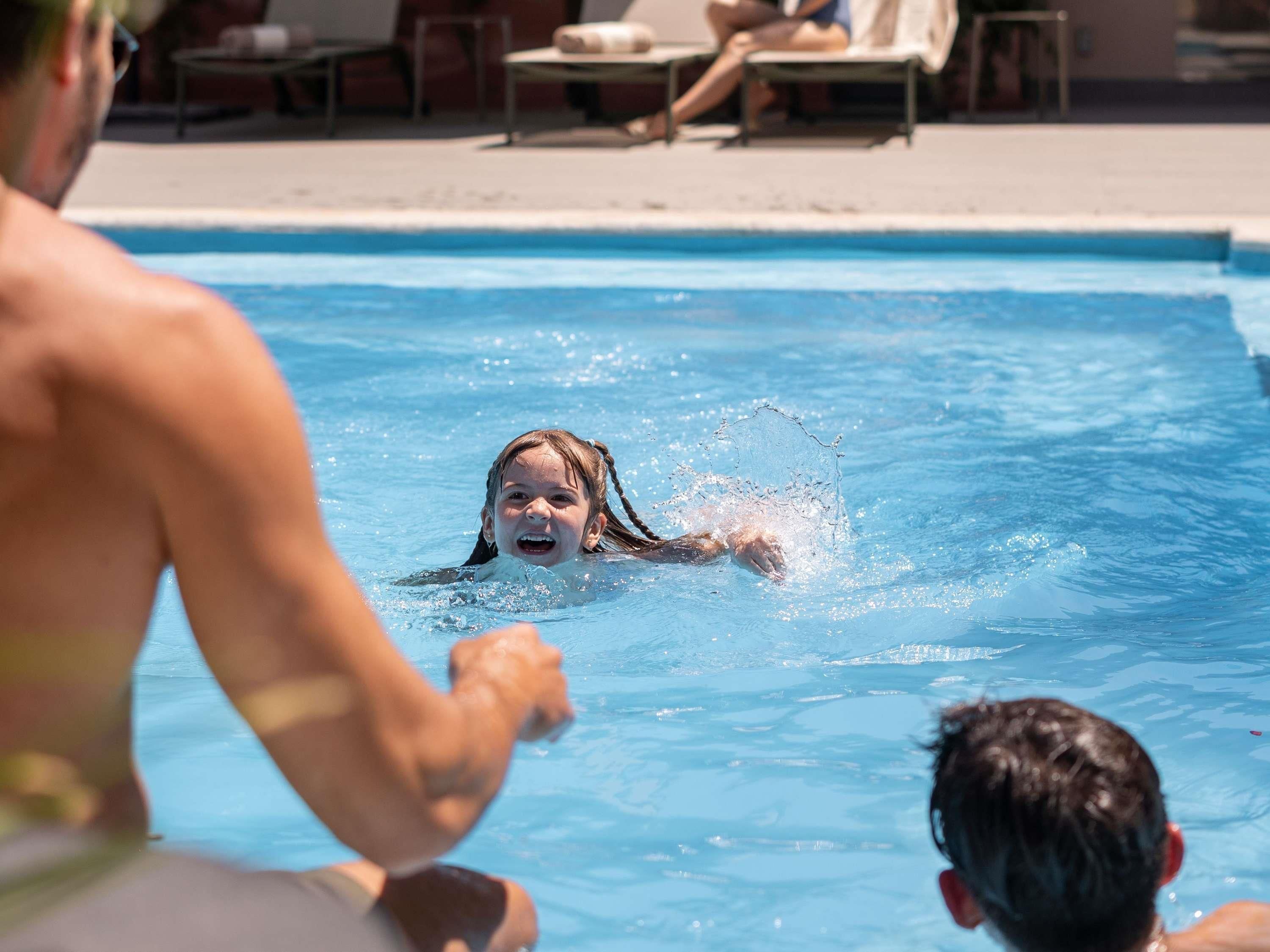 Una piscina con sillones de descanso y una persona nadando.
