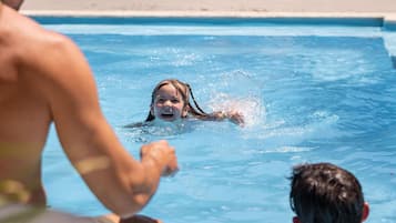 Una piscina con sillones de descanso y una persona nadando.