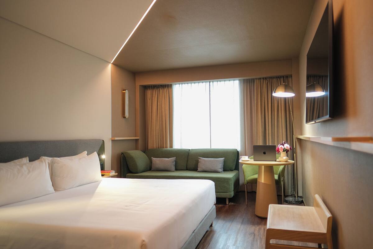 Habitación de hotel con una cama grande, un sofá verde, una mesita con una computadora portátil y una silla.