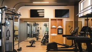 Une salle de sport équipée de matériel d’exercice, dotée d’un miroir et d’un mur en bois sur lequel est fixée une télévision.