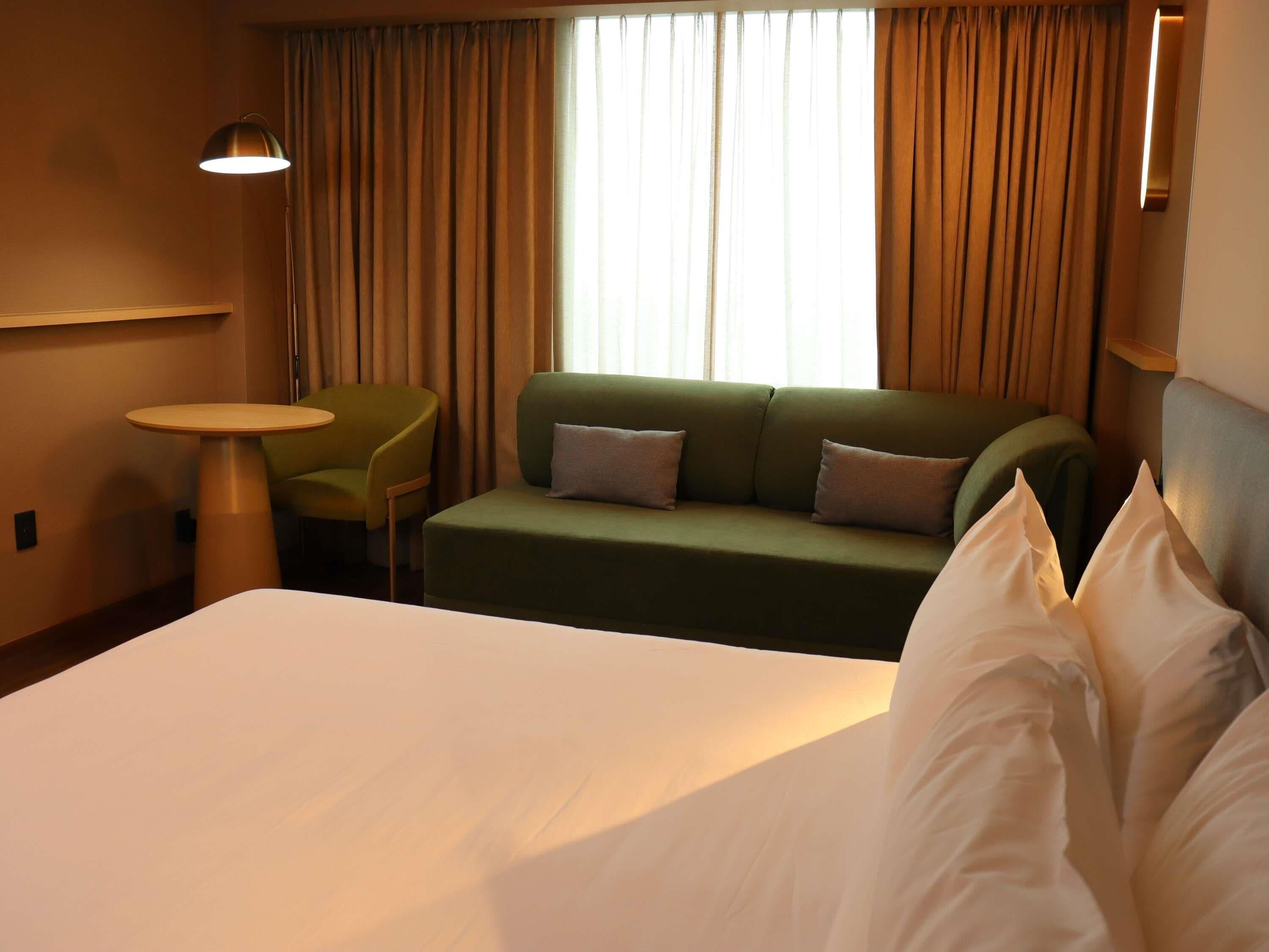 Une chambre d’hôtel avec un lit, un canapé vert, une petite table ronde et une lampe.