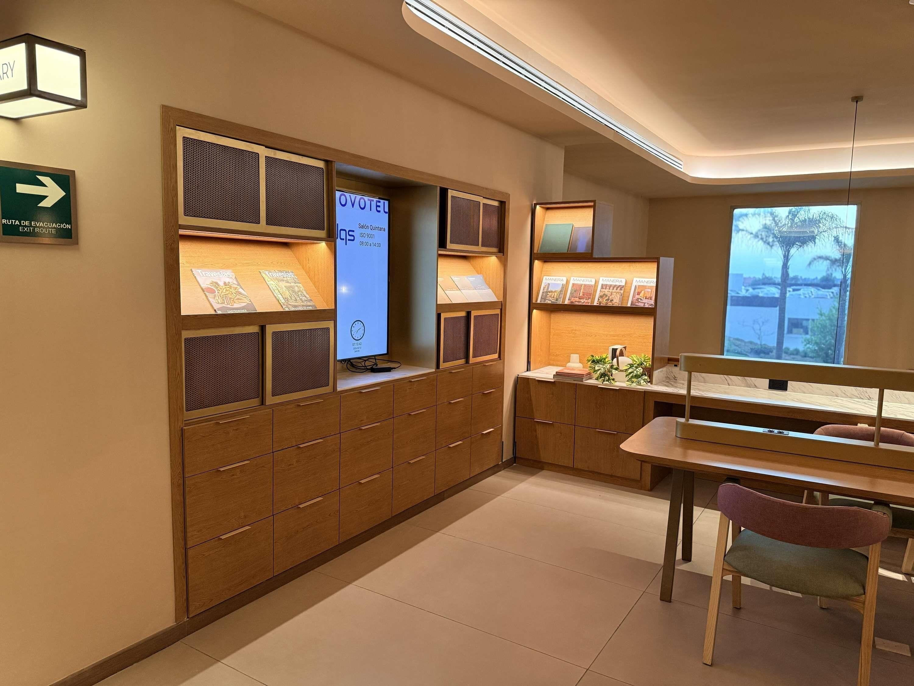 A hotel lobby with a reception desk, a digital display, a clock, and a window with a view.