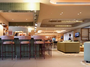 A modern bar area with high stools, a counter, and a seating area with a sofa and armchairs.