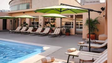 Un área junto a la piscina con sillones reclinables, sombrillas y una piscina.