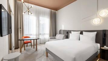 Habitación de hotel con cama, televisor, escritorio y silla, y ventana con cortinas.