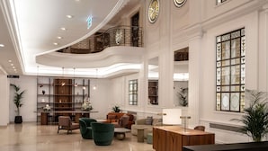 A spacious lobby with a high ceiling, a central seating area, a reception desk, and large windows with decorative glass. - Mövenpick Hotel Budapest Centre (Budapest)