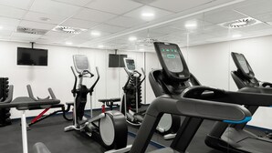A modern gym with various exercise machines, including treadmills and stationary bikes, and a flat-screen TV mounted on the wall. - Mövenpick Hotel Budapest Centre (Budapest)