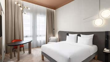 A hotel room with a bed, a desk, a chair, a telephone, and a wall-mounted light fixture.