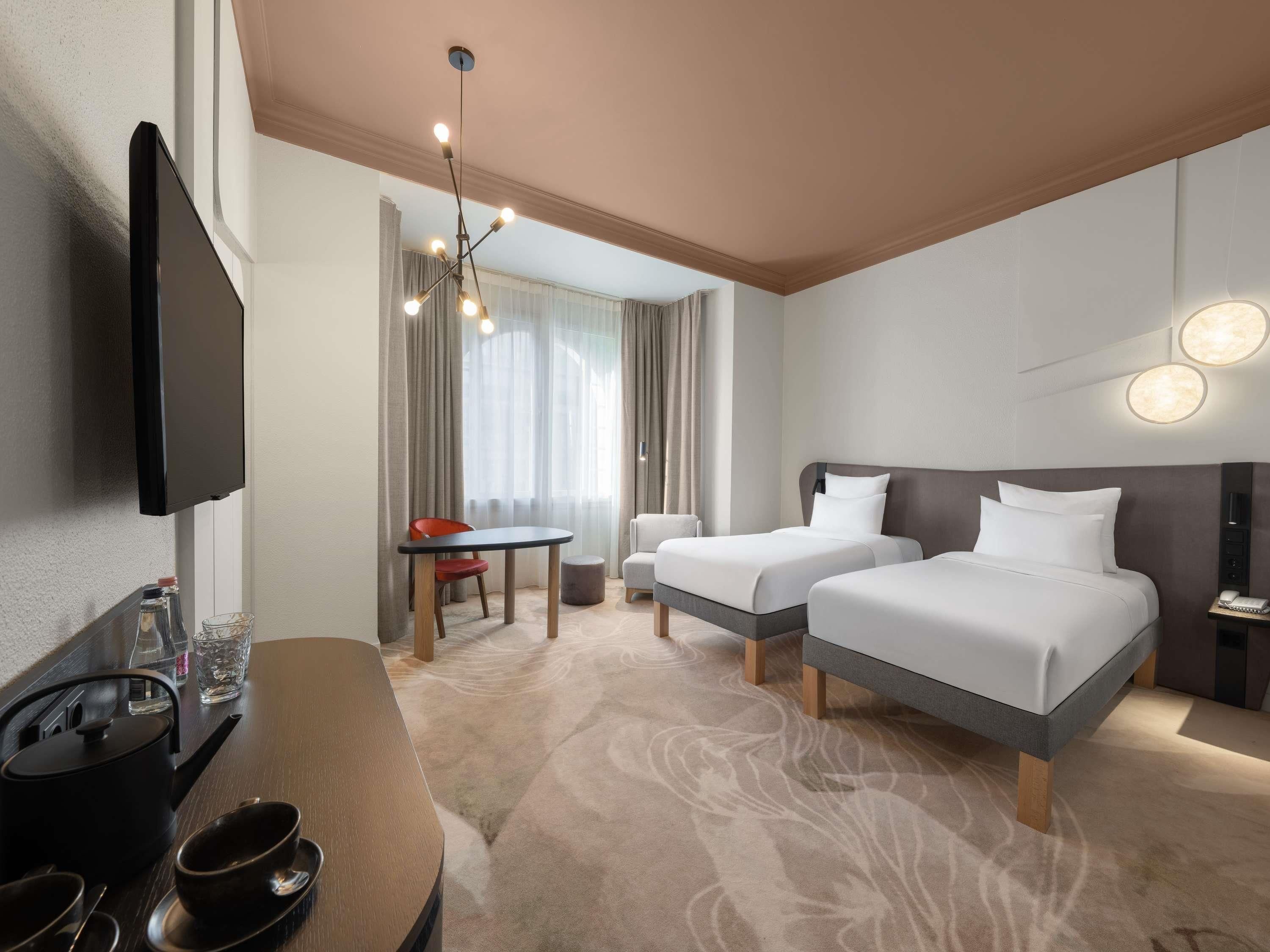 A hotel room with two beds, a TV, a dining table, and a chandelier.