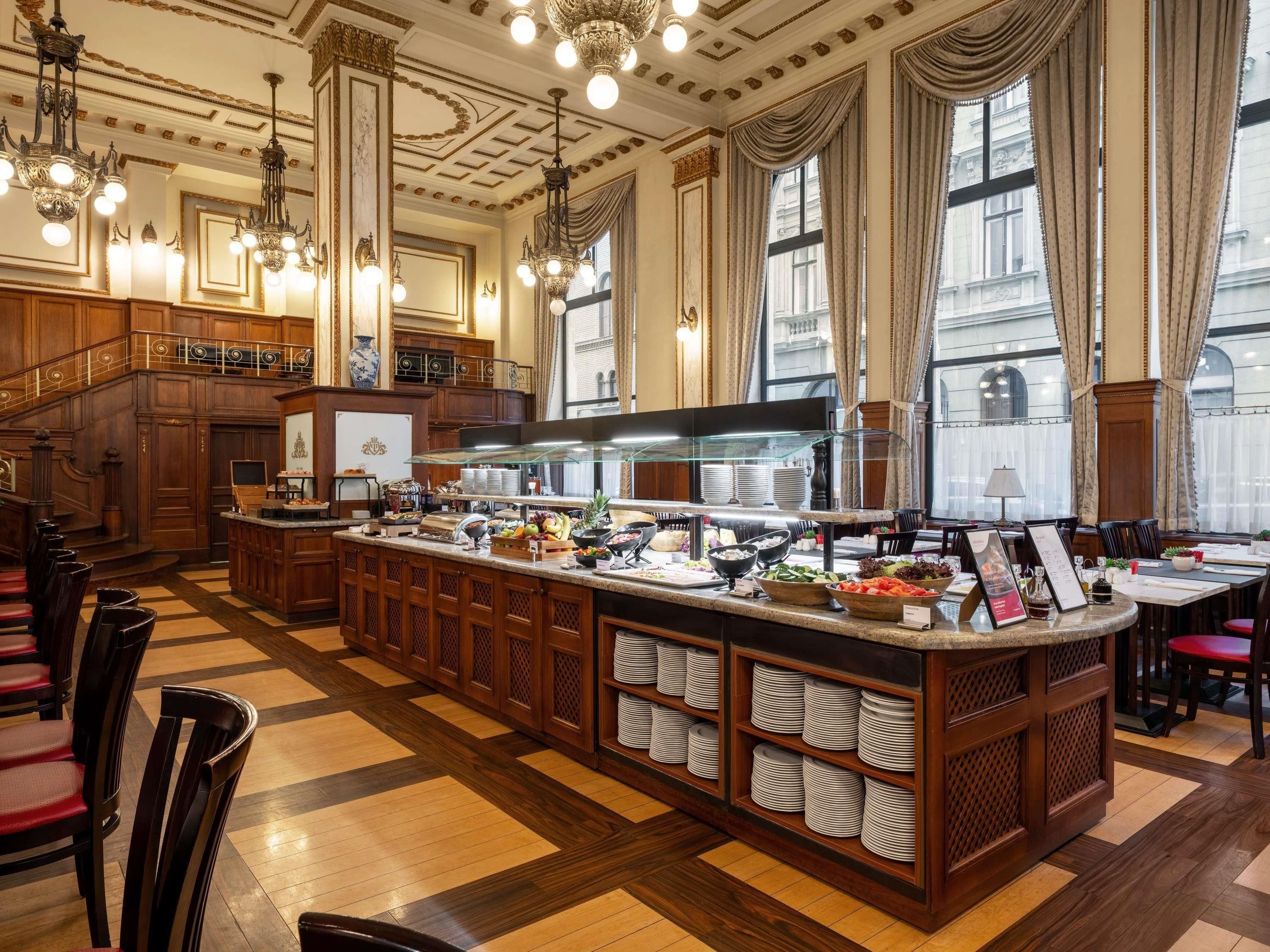 Eine Hotelhalle mit Frühstücksbuffet, Holzböden, Kronleuchtern und großen Fenstern.