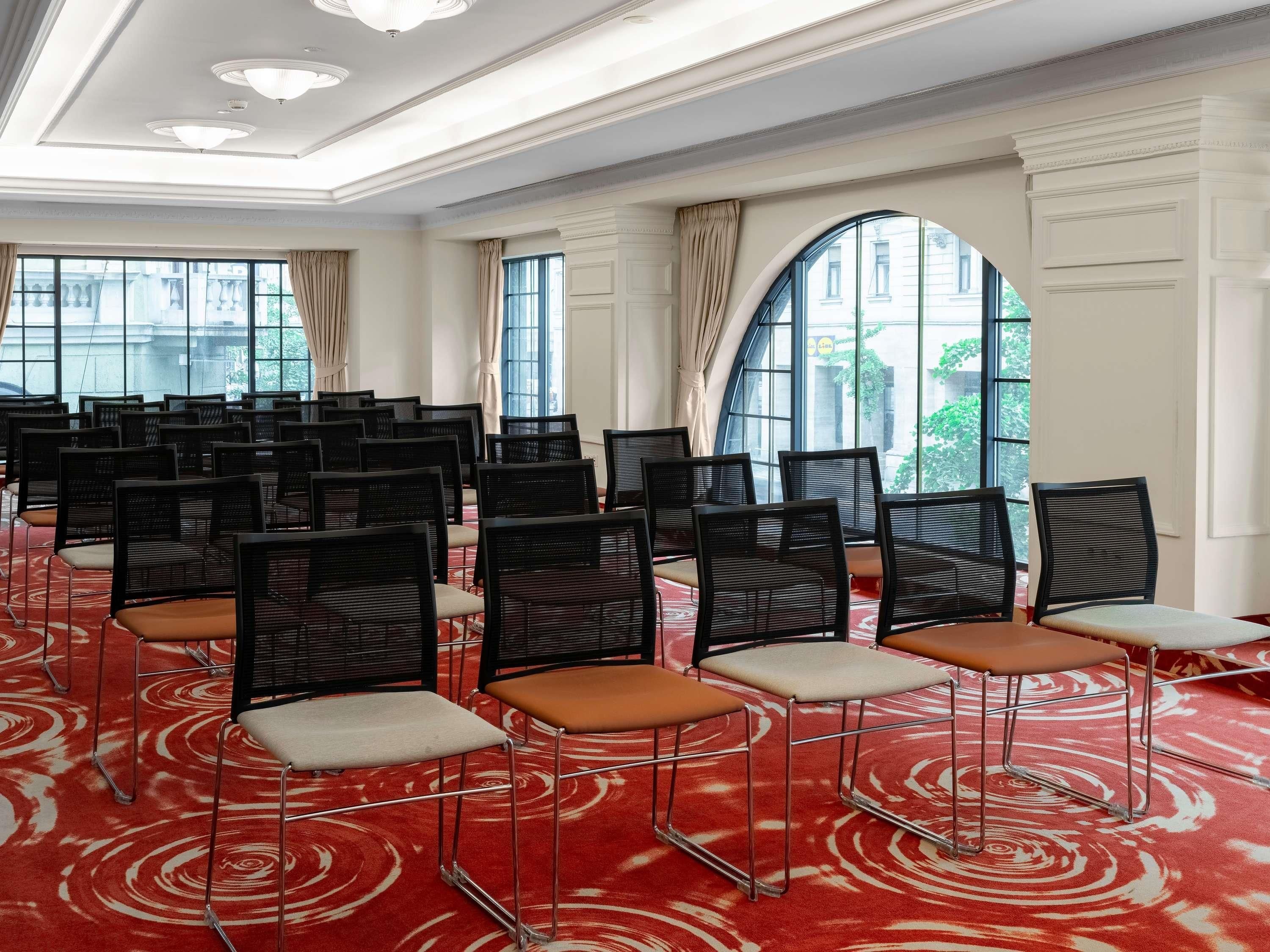 A conference room with rows of chairs, large windows, and a red carpet.