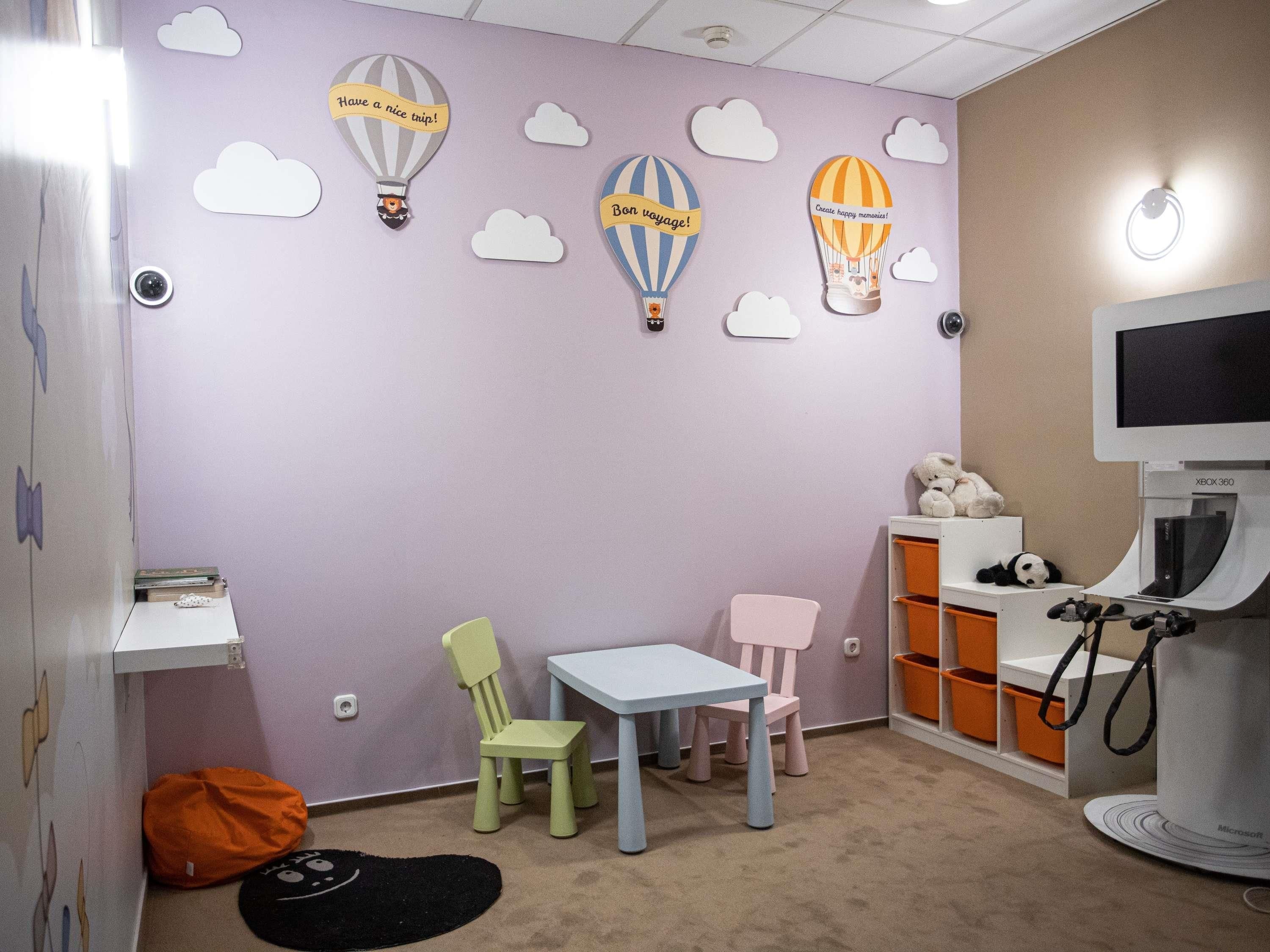 A children's playroom with a purple wall, hot air balloon decorations, a small table, chairs, and a gaming console.