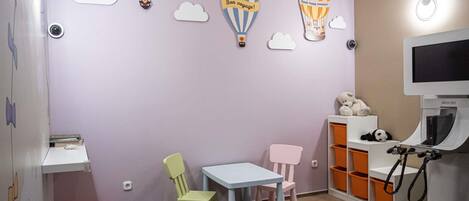 Una sala de juegos para niños con una pared morada, decoraciones de globos aerostáticos, una mesita, sillas y una consola de videojuegos.