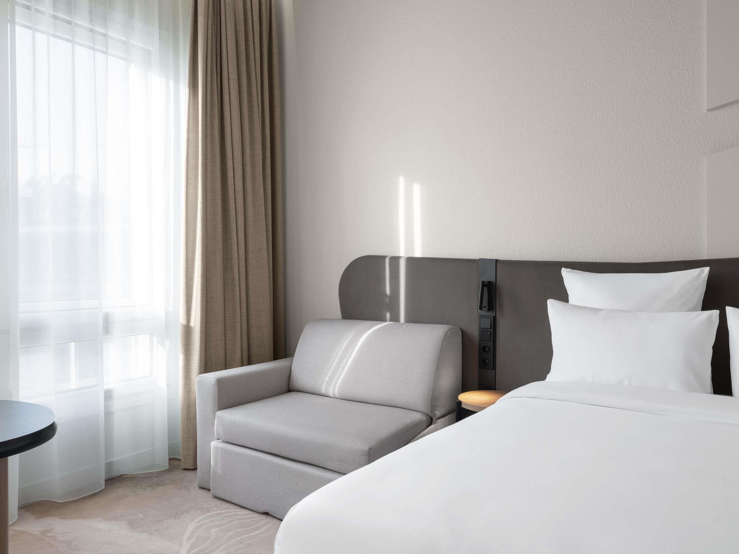 Habitación de hotel con cama, una silla, una mesita y una lámpara fijada a la pared.