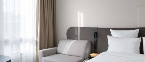 Habitación de hotel con cama, una silla, una mesita y una lámpara fijada a la pared.