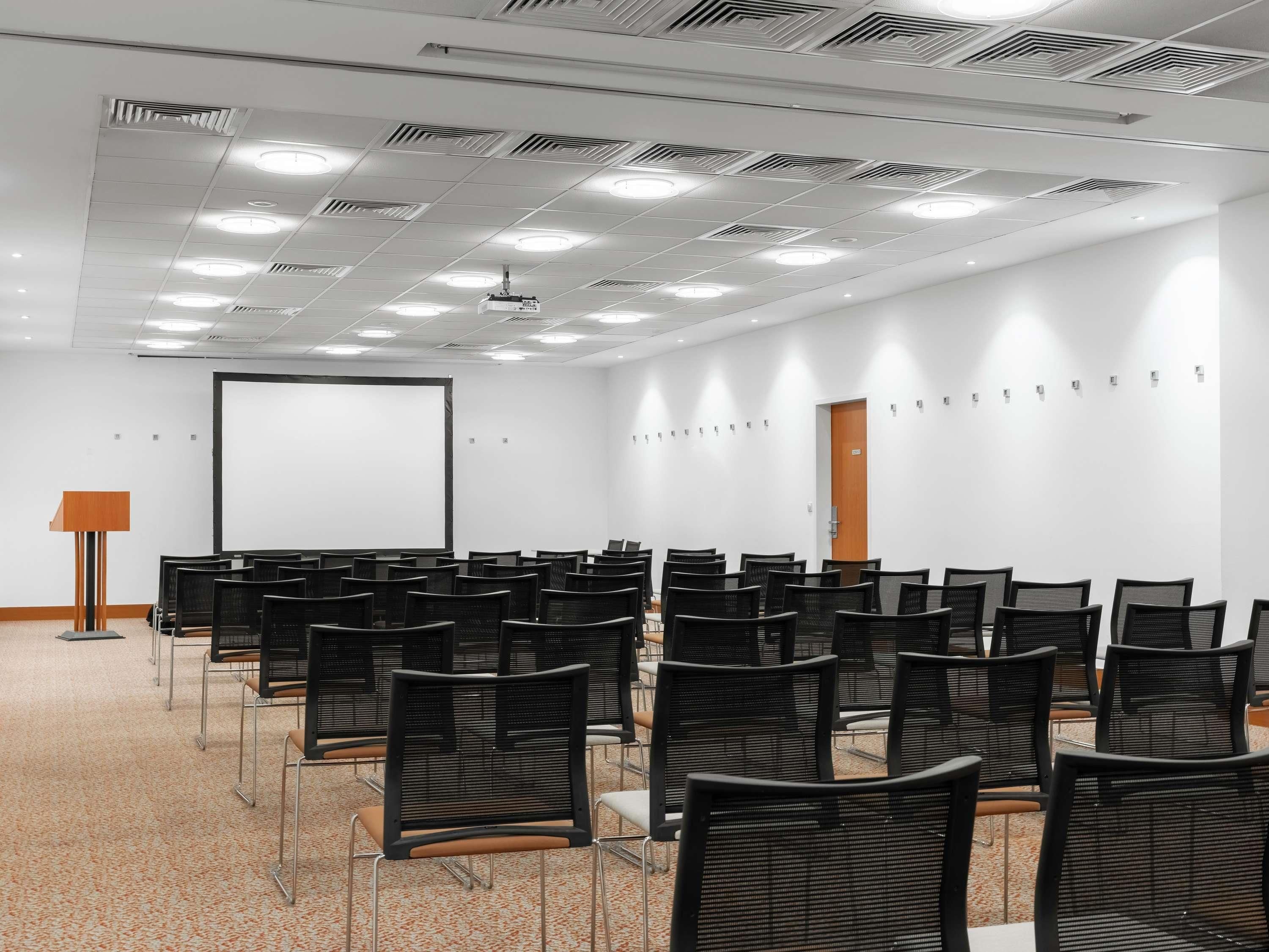 A conference room with rows of chairs, a projector screen, and a podium.