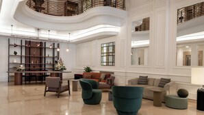A spacious lobby with a high ceiling, a central seating area with modern chairs, a bar area with shelves, and a staircase leading to an upper level. - Mövenpick Hotel Budapest Centre (Budapest)