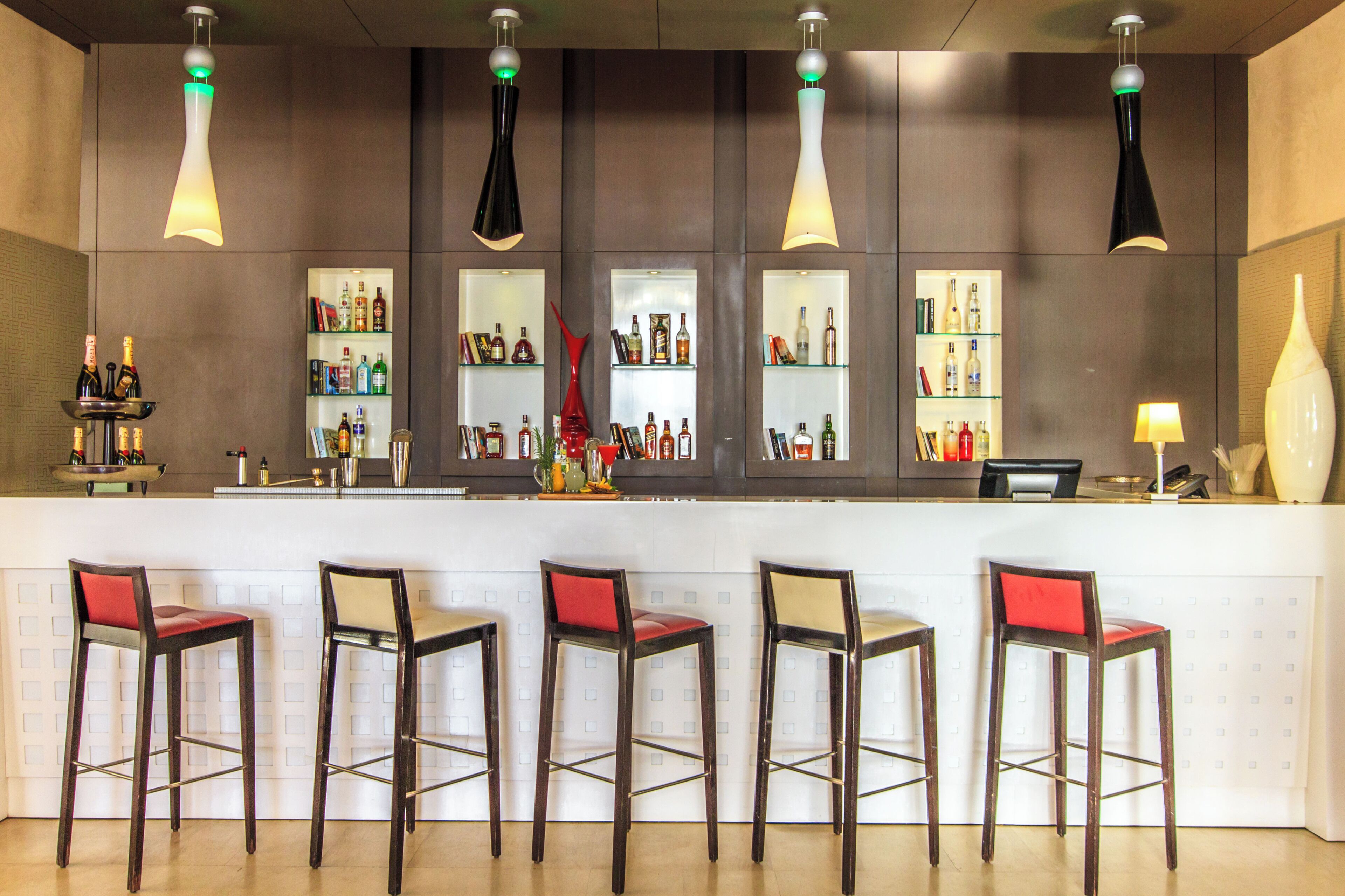 A bar area with five stools, a counter with shelves of bottles, and hanging pendant lights.