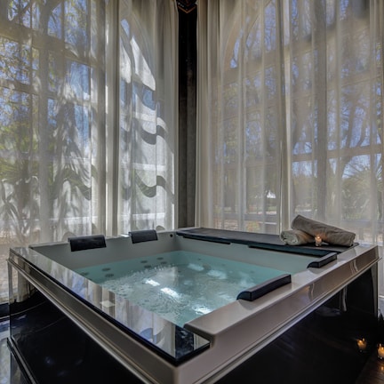 A spa room with a glass-enclosed hot tub, sheer curtains, and a robe rack.