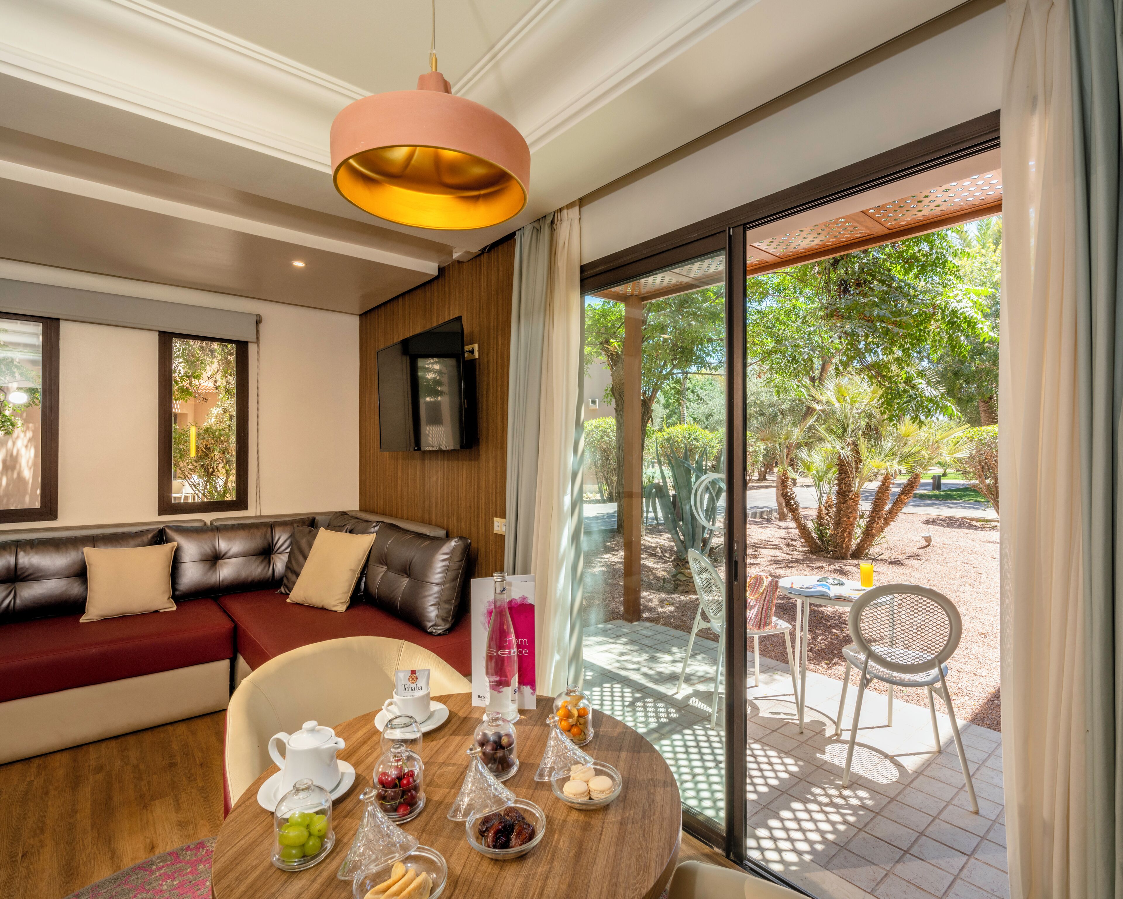 Ein modernes Wohnzimmer mit einer Ledersofa, einem Esstisch mit verschiedenen Snacks und einem großen Fenster mit Blick auf einen Garten.
