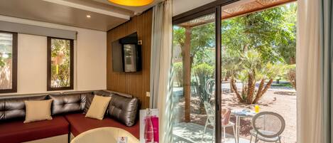 A modern living room with a leather sofa, a dining table with various snacks, and a large window overlooking a garden.
